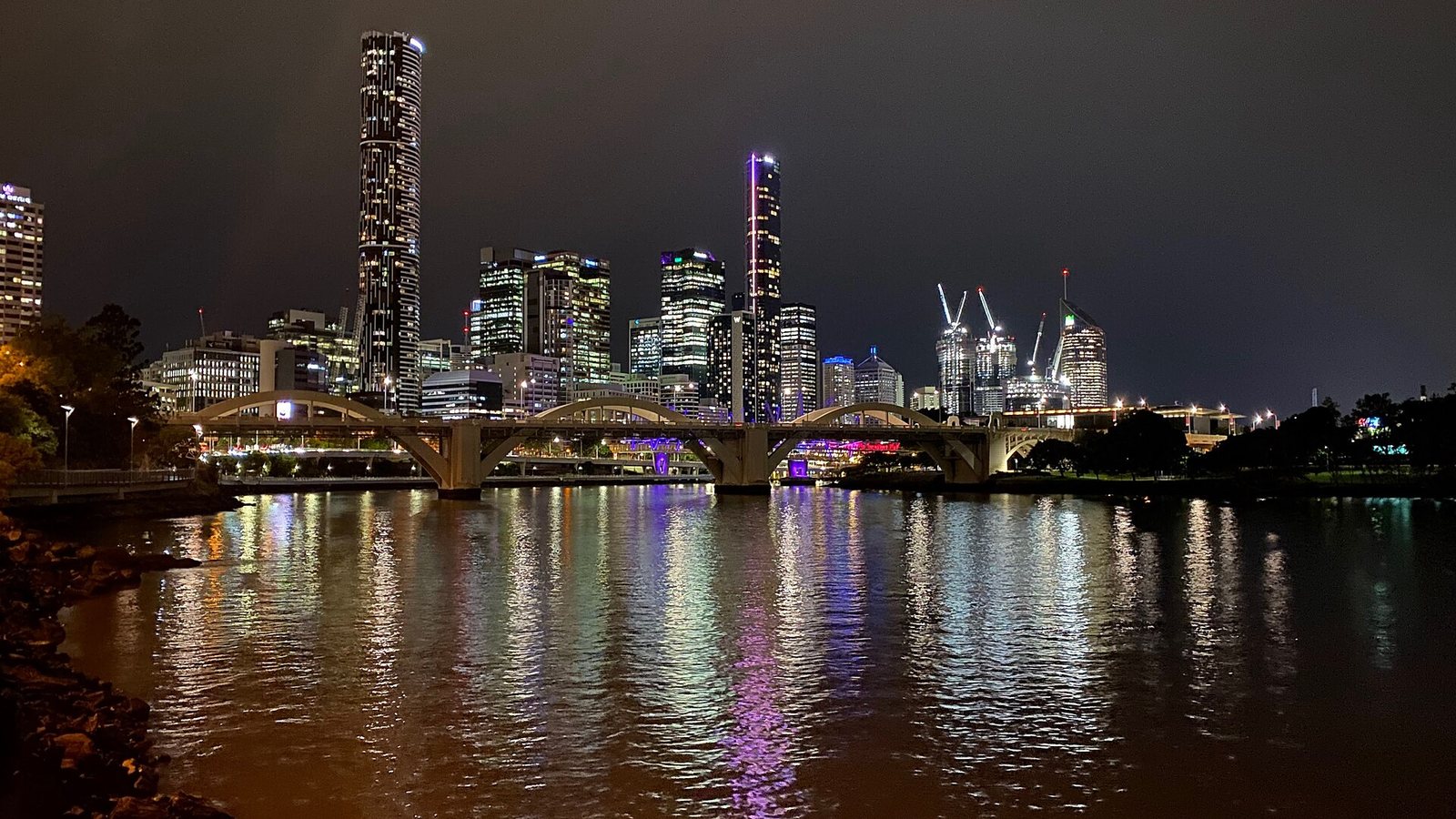 The Brisbane city skyline and an arched bridge reflected in the Brisbane River at night