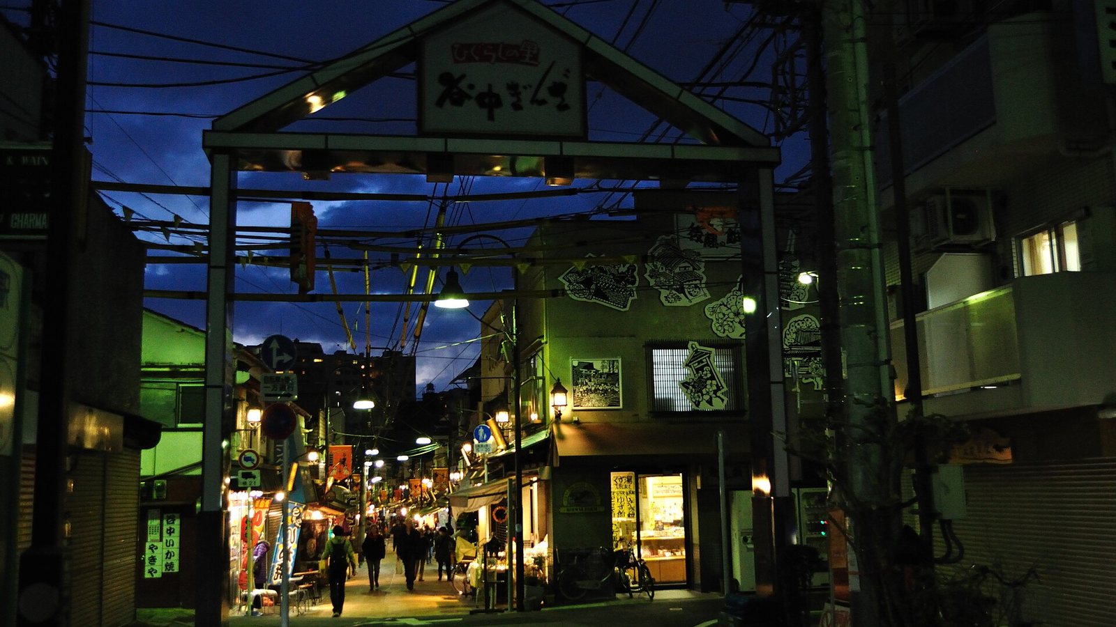 The entrance gate and lit shops of the Yanaka Ginza shopping street in Tokyo at dusk