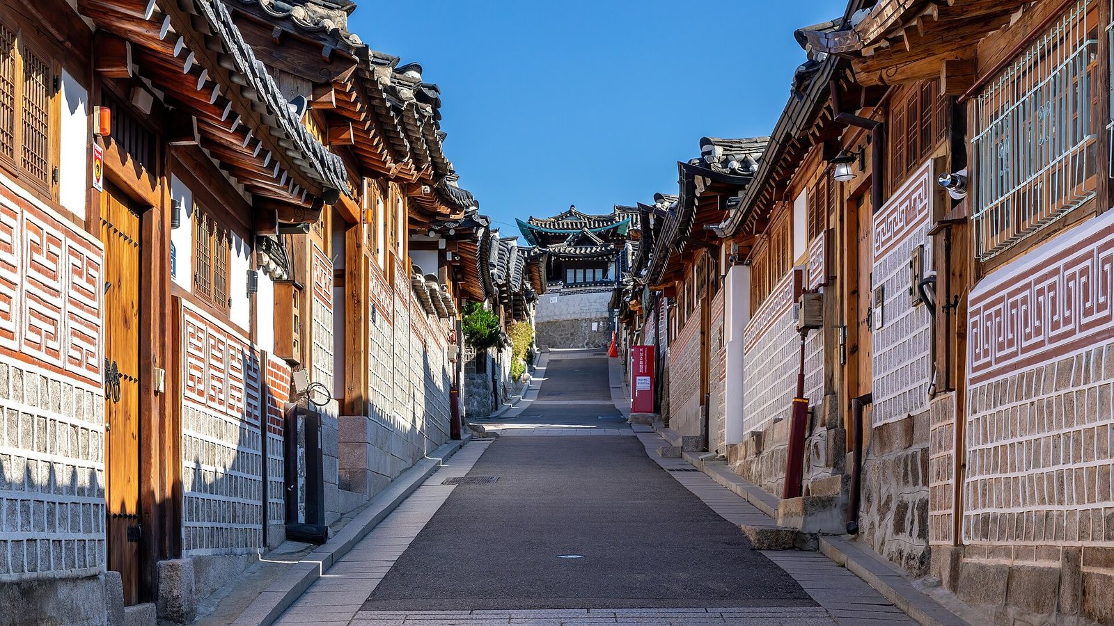 A sloping street lined with traditional hanok houses in Bukchon Hanok Village, Seoul, under a blue sky