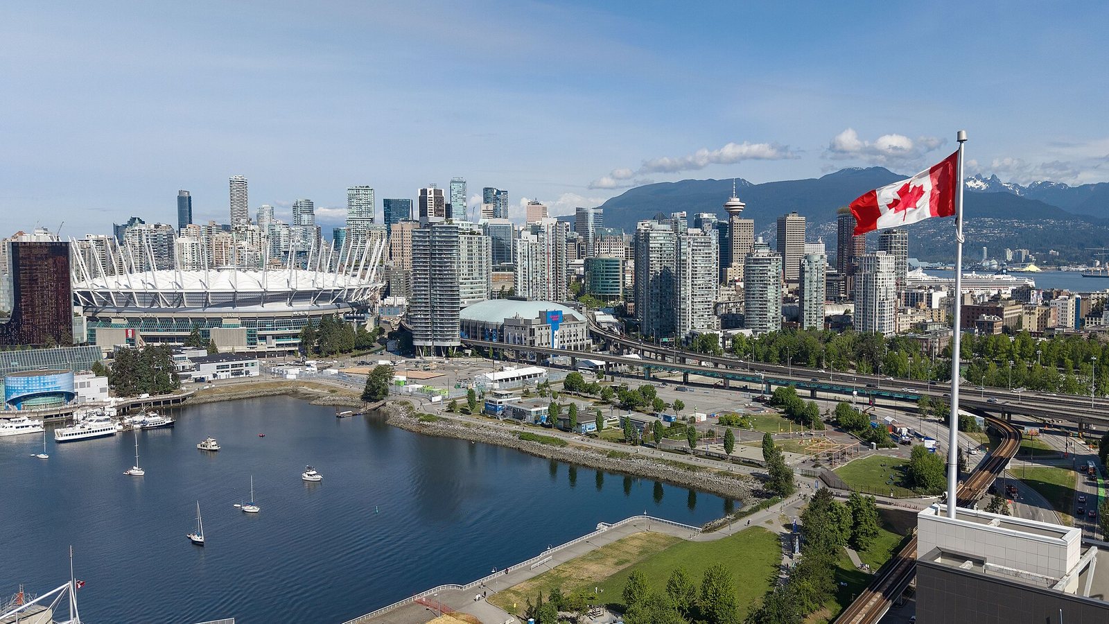 Downtown Vancouver and False Creek with a Canadian flag in the foreground and mountains behind