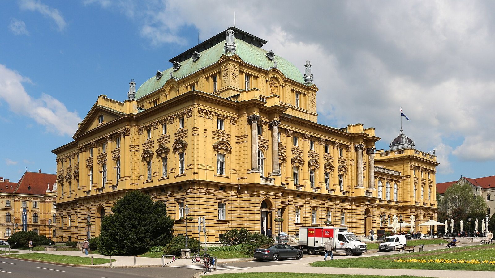 The yellow neo-baroque building of the Croatian National Theatre in Zagreb with its green copper dome, under a blue sky with white clouds