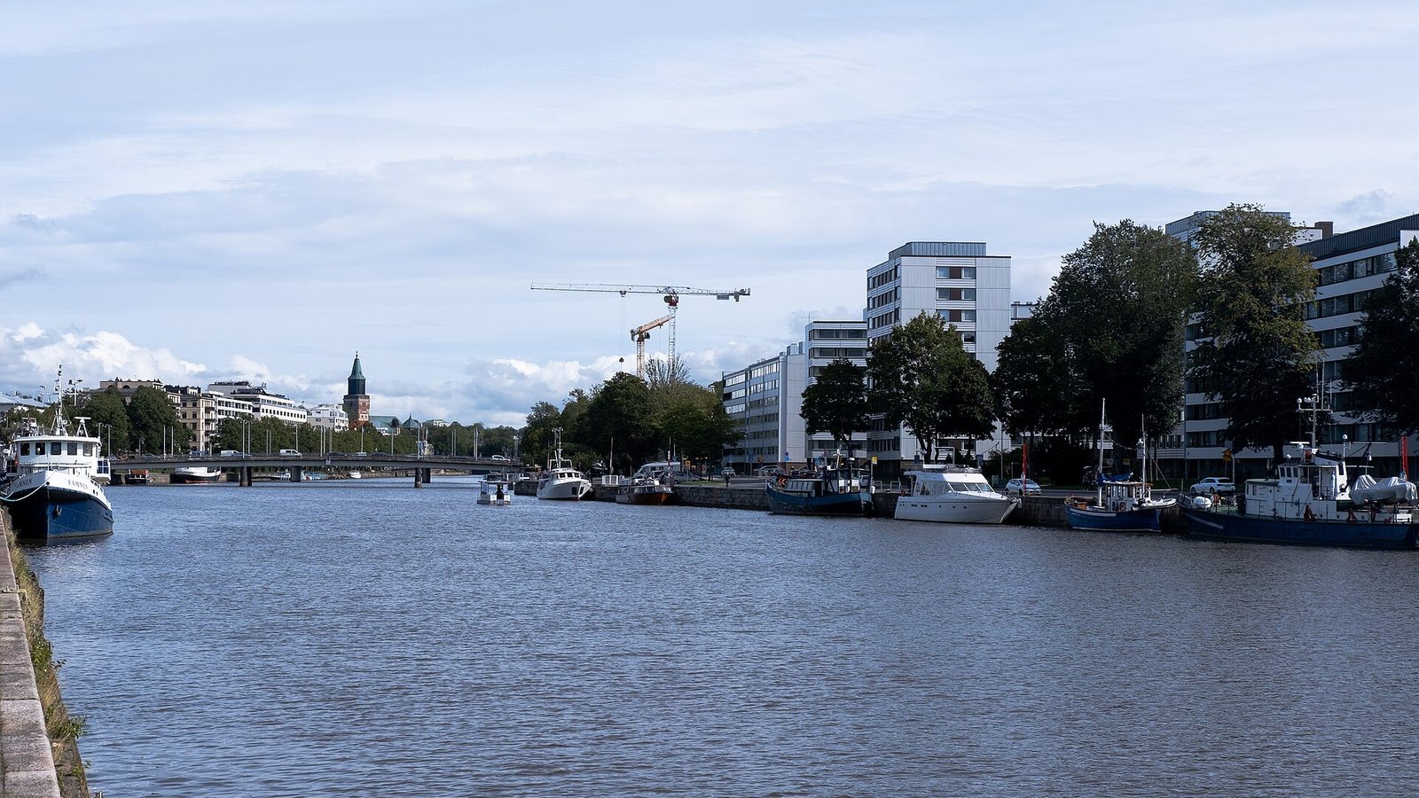 Boats moored along the Aura river in Turku, Finland, with the cathedral tower in the distance