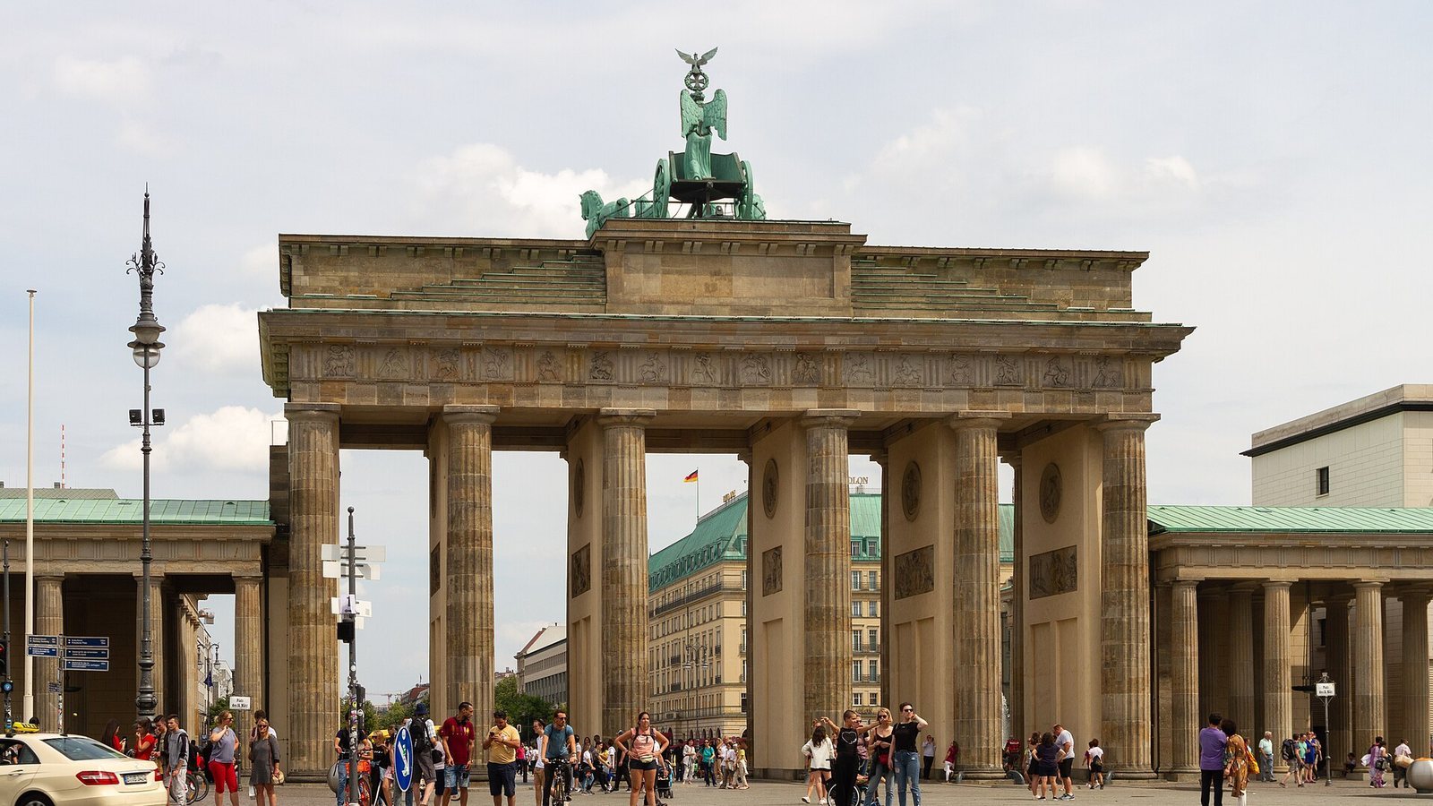The Brandenburg Gate in Berlin with its quadriga, seen from Pariser Platz with pedestrians on a partly cloudy day