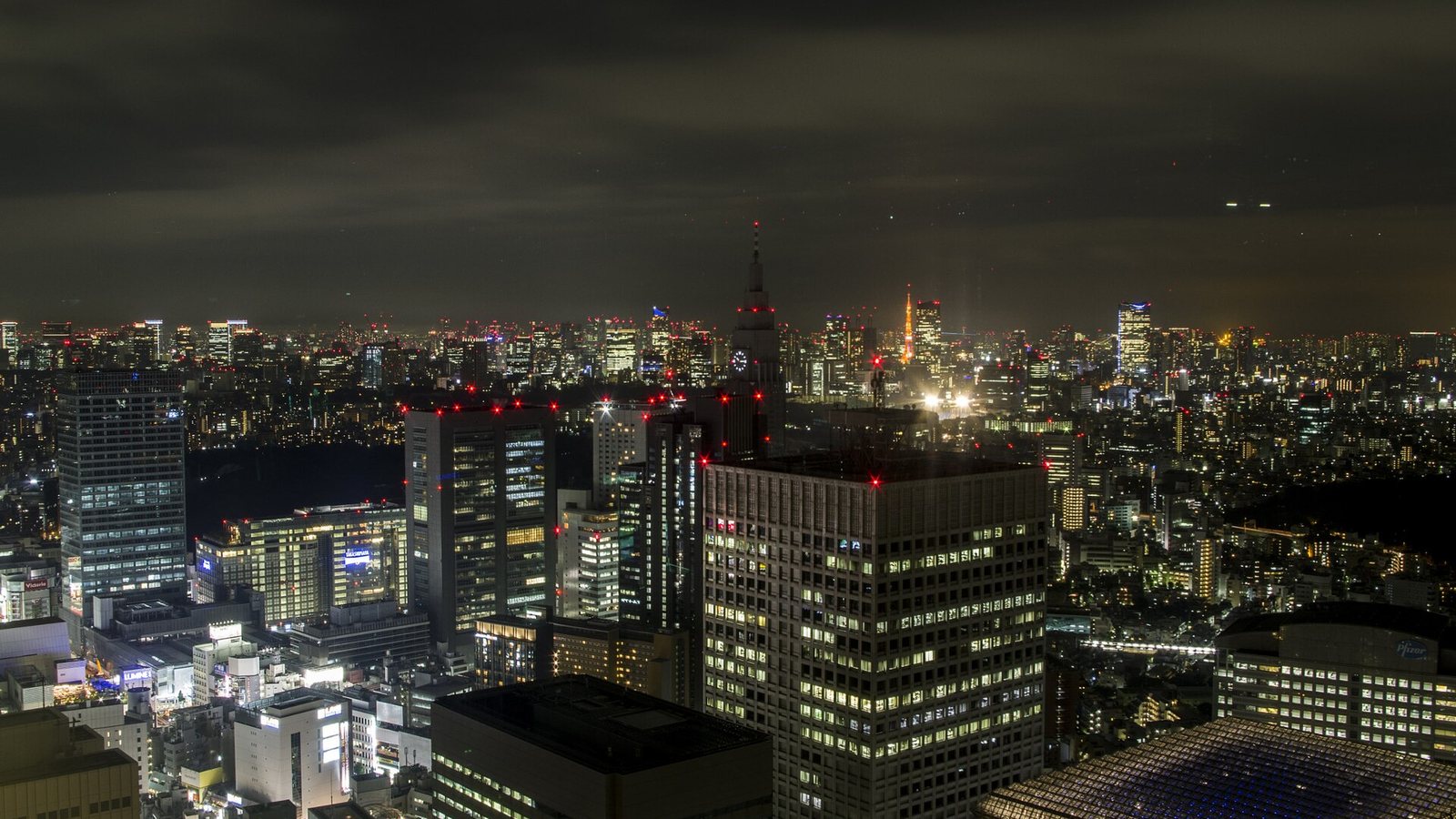 The Shinjuku skyline in Tokyo at night, with Tokyo Tower lit in the distance