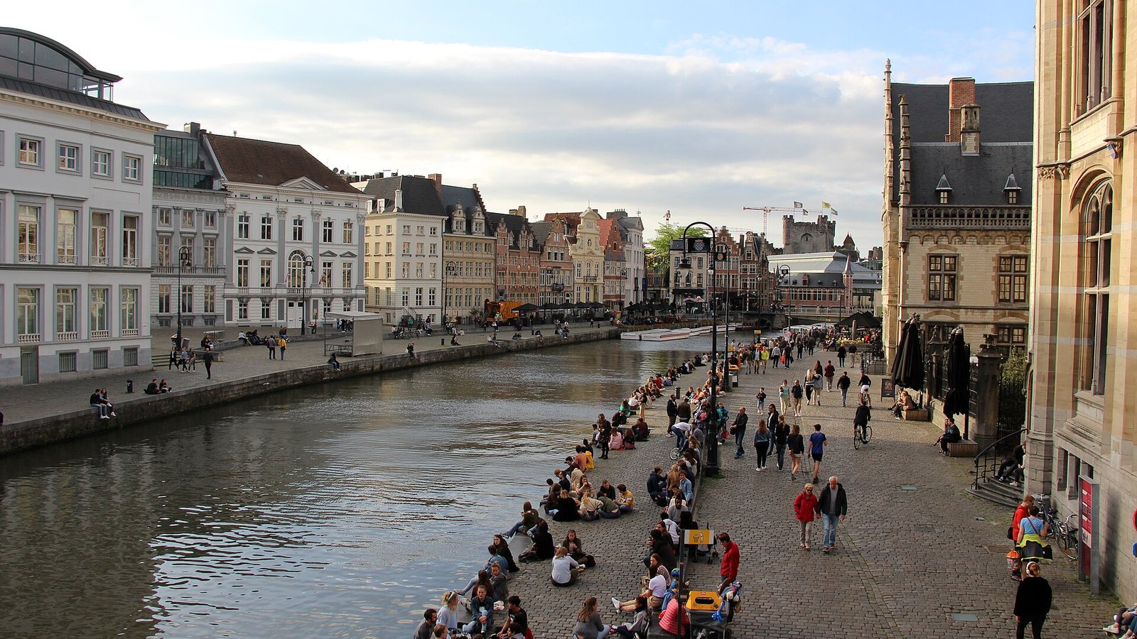The Graslei and Korenlei quays in Ghent, with people sitting along the river Leie and rows of historic guild houses on both banks