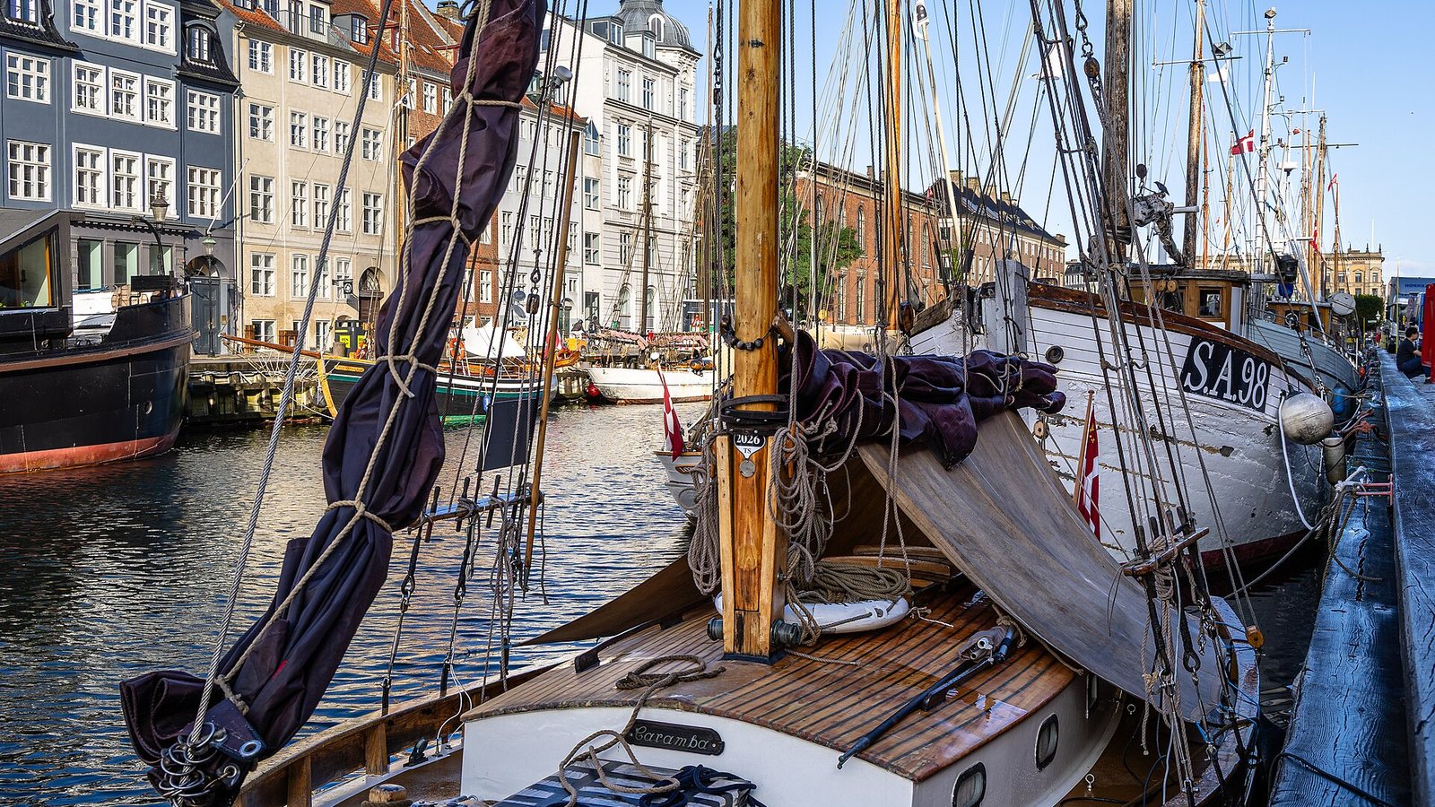 Colourful gabled townhouses and moored wooden sailing ships along the Nyhavn canal in Copenhagen under a blue sky