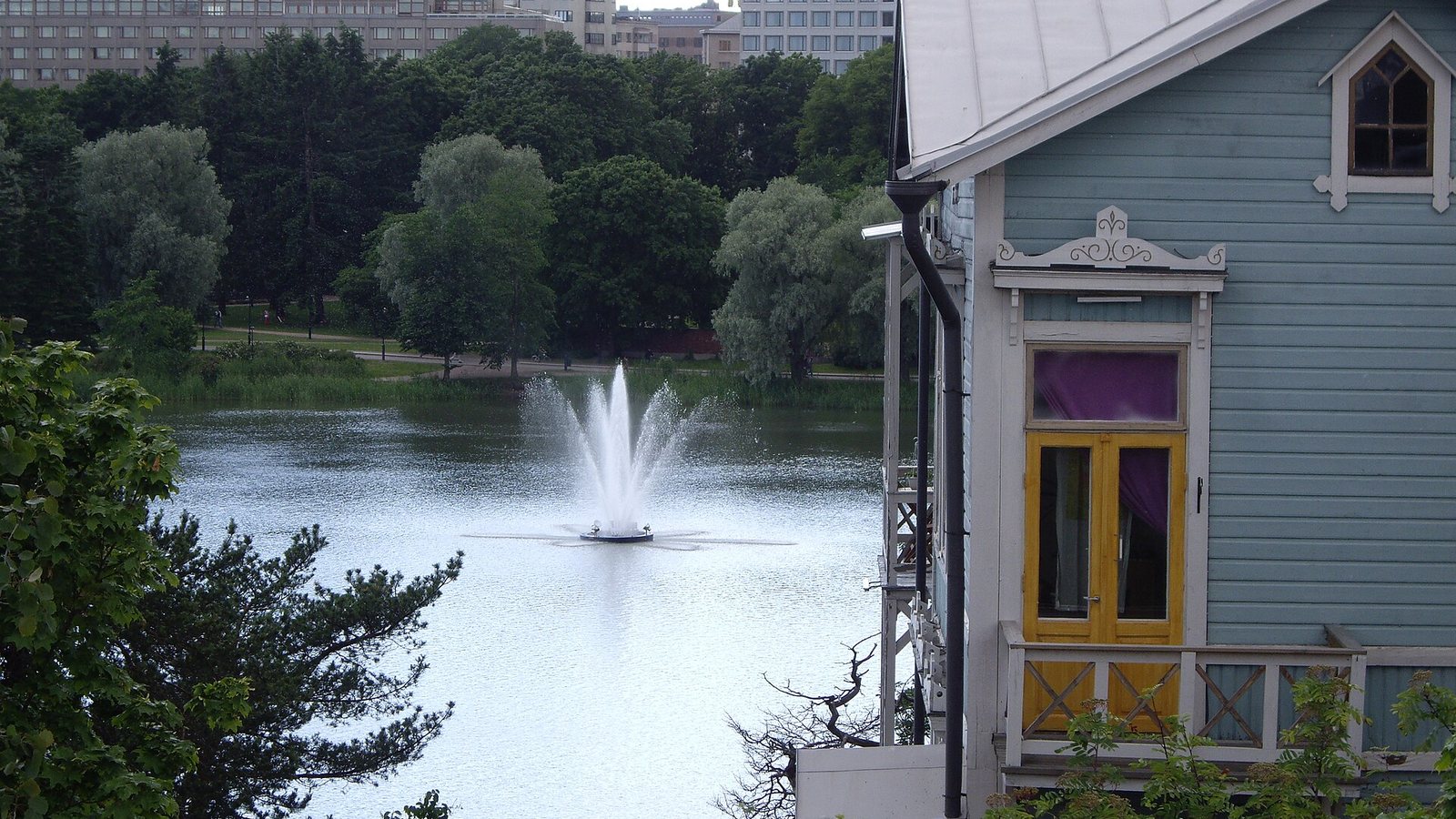 A blue wooden villa overlooking Töölönlahti bay and its fountain in Helsinki in summer