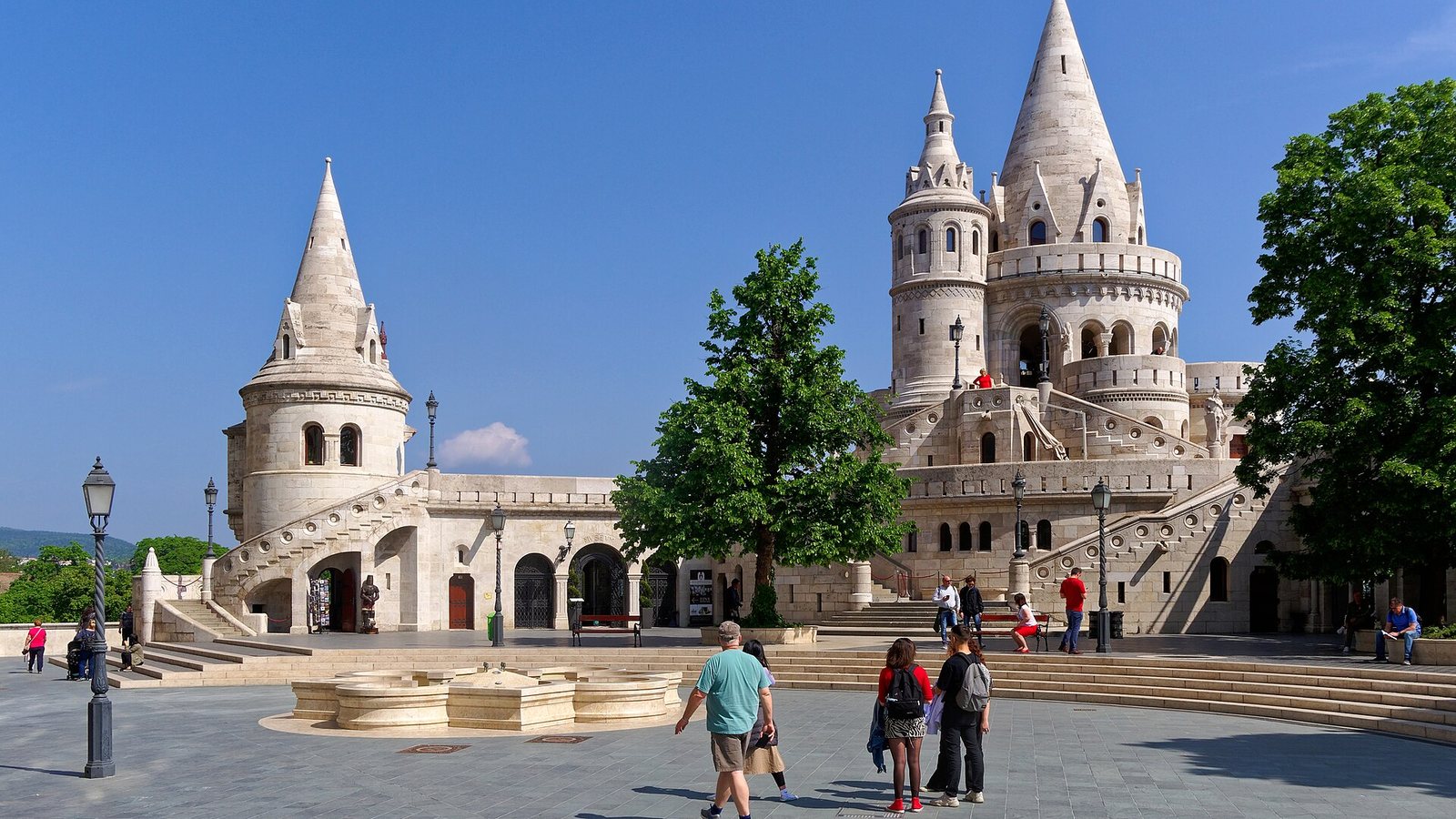The white towers and staircases of Fisherman's Bastion in Budapest under a deep blue sky, with visitors walking across the square