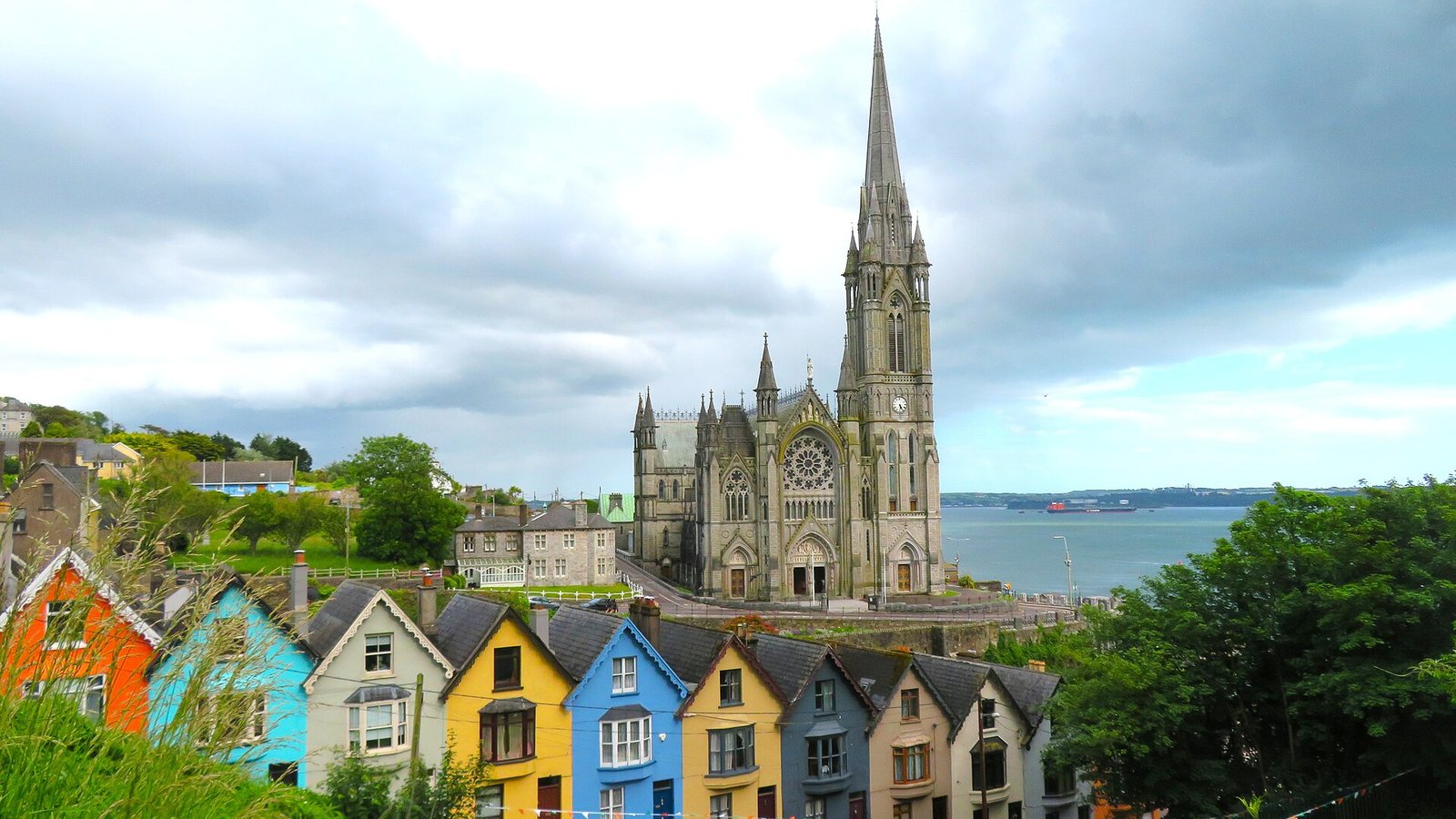 A row of brightly painted terraced houses below St Colman's Cathedral in Cobh, County Cork, with the harbour behind