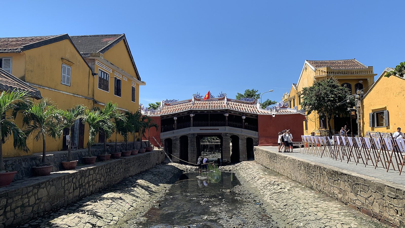 The Japanese Covered Bridge in Hoi An with its tiled roof and red walls, between yellow colonial houses under a clear blue sky