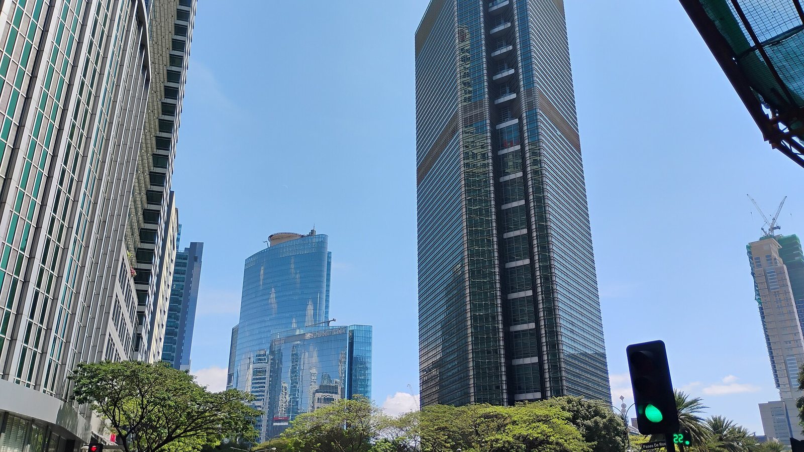 Glass office towers in the Makati business district seen from Ayala Triangle under a blue sky