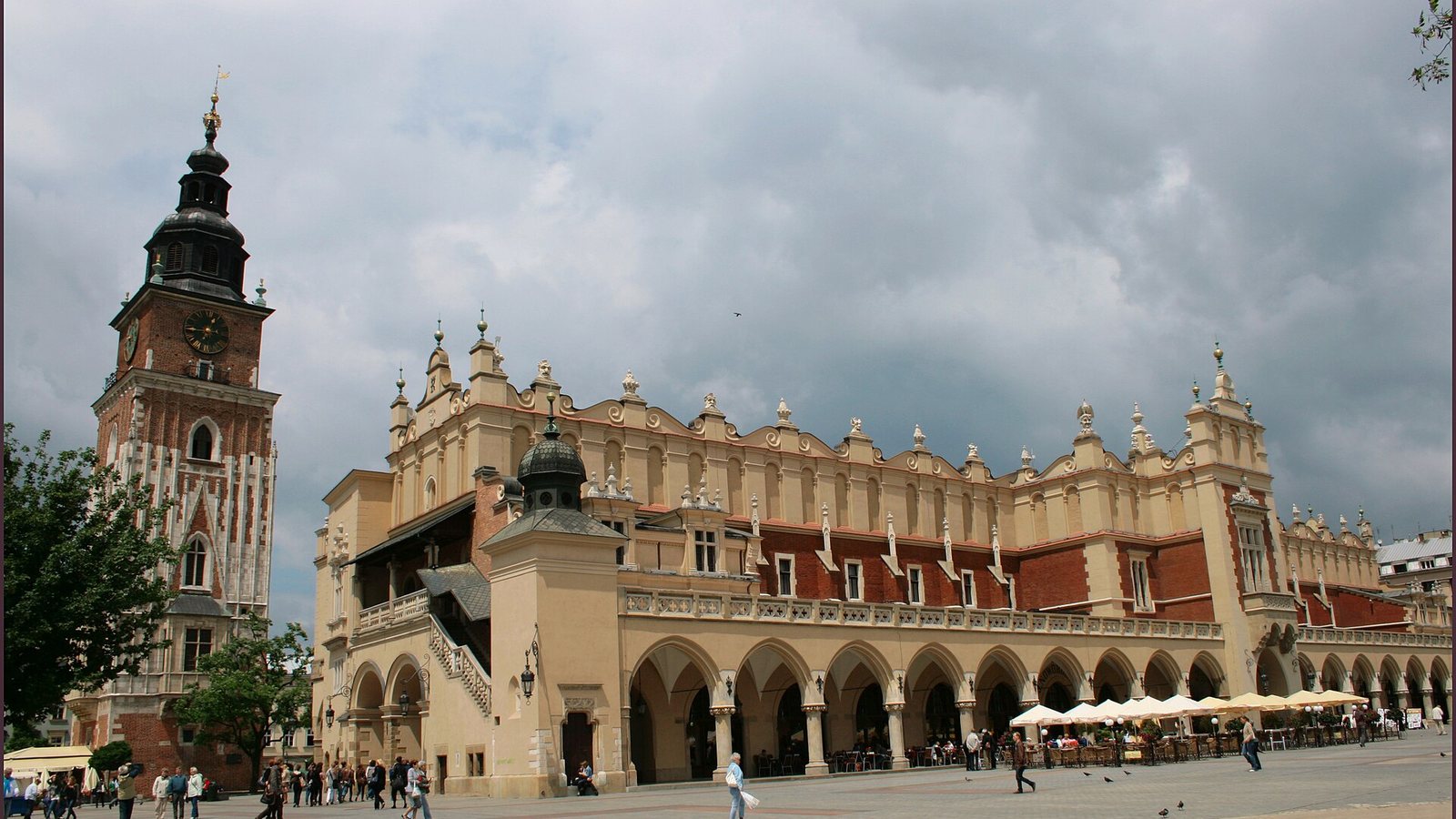 The Cloth Hall and Town Hall Tower on the Main Market Square in Kraków, with people crossing the square under a cloudy sky