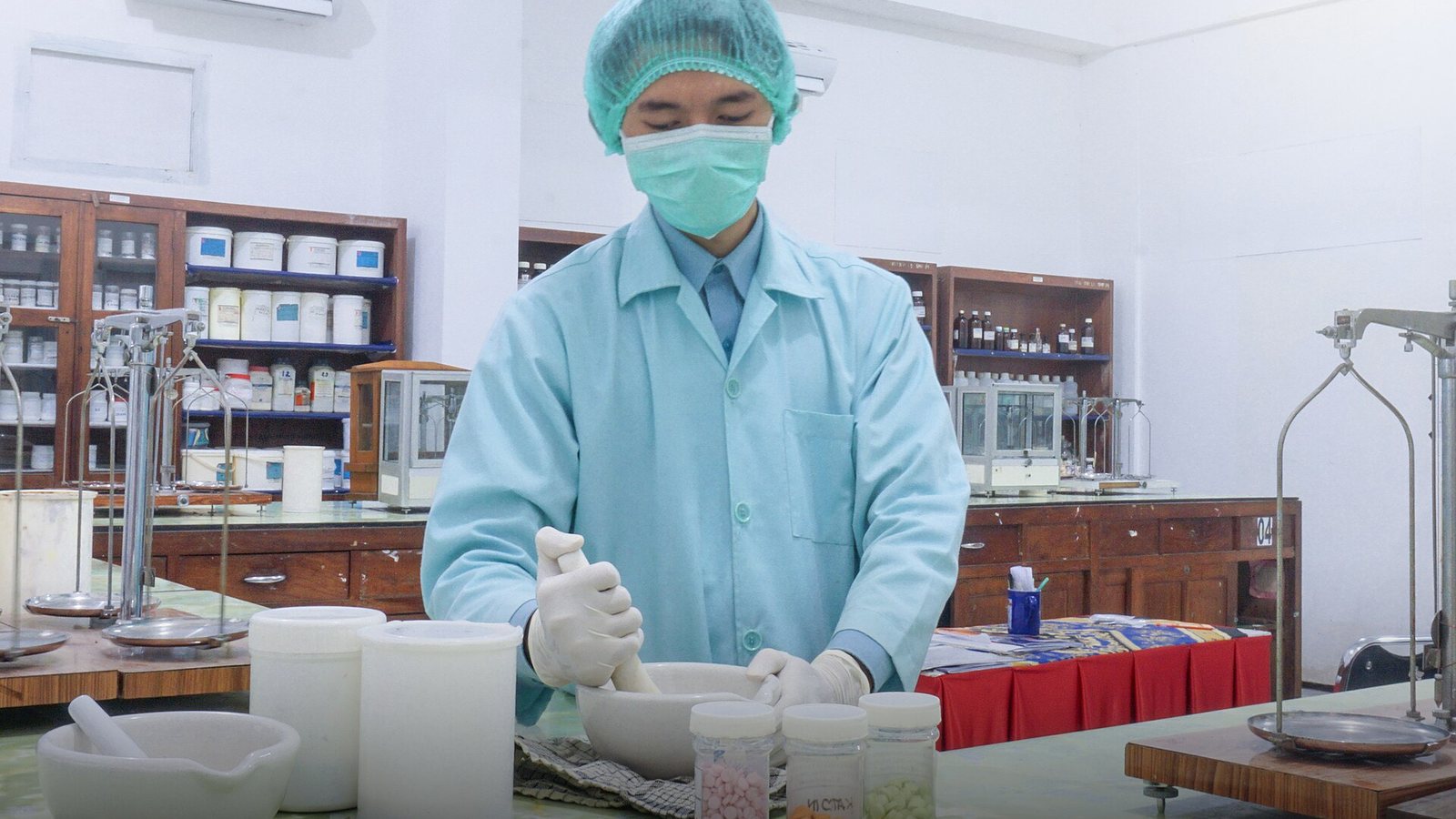 A pharmacy assistant in protective clothing preparing medicine with a mortar and pestle