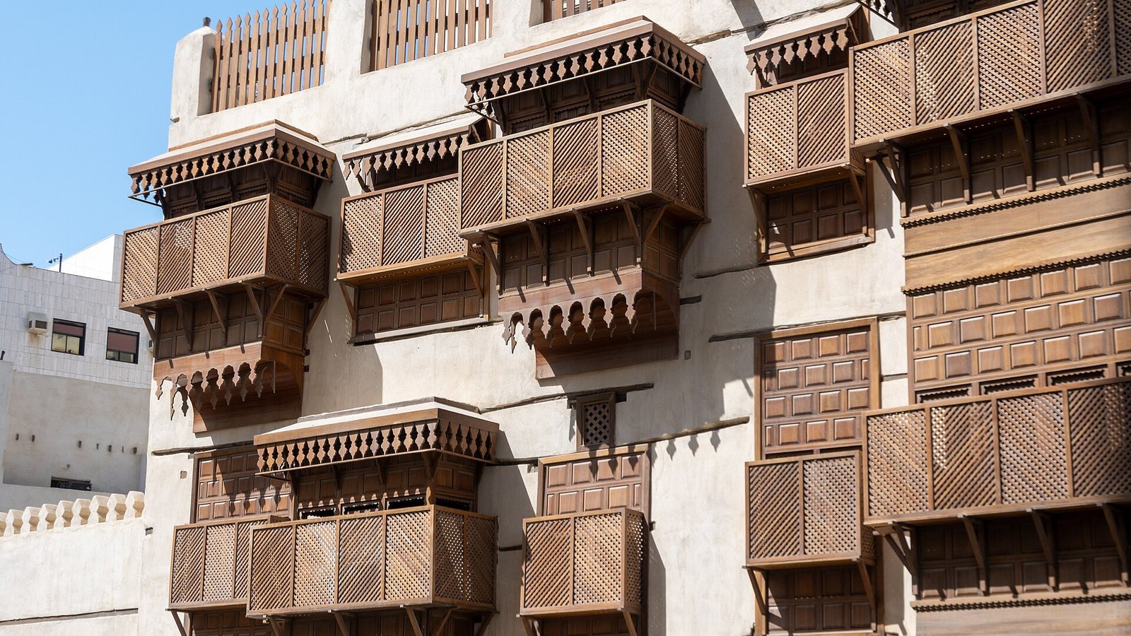 Coral-stone building in Old Jeddah with tiers of carved wooden rawasheen balconies and latticed window screens in bright sunlight