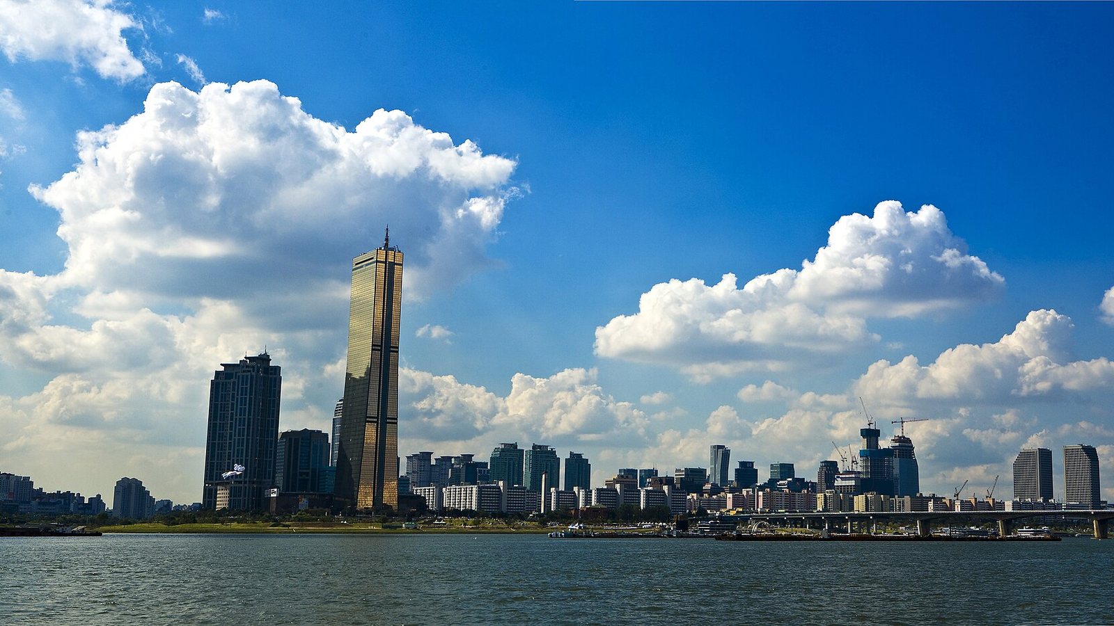 The Yeouido business district of Seoul seen across the Han River under a blue sky with clouds