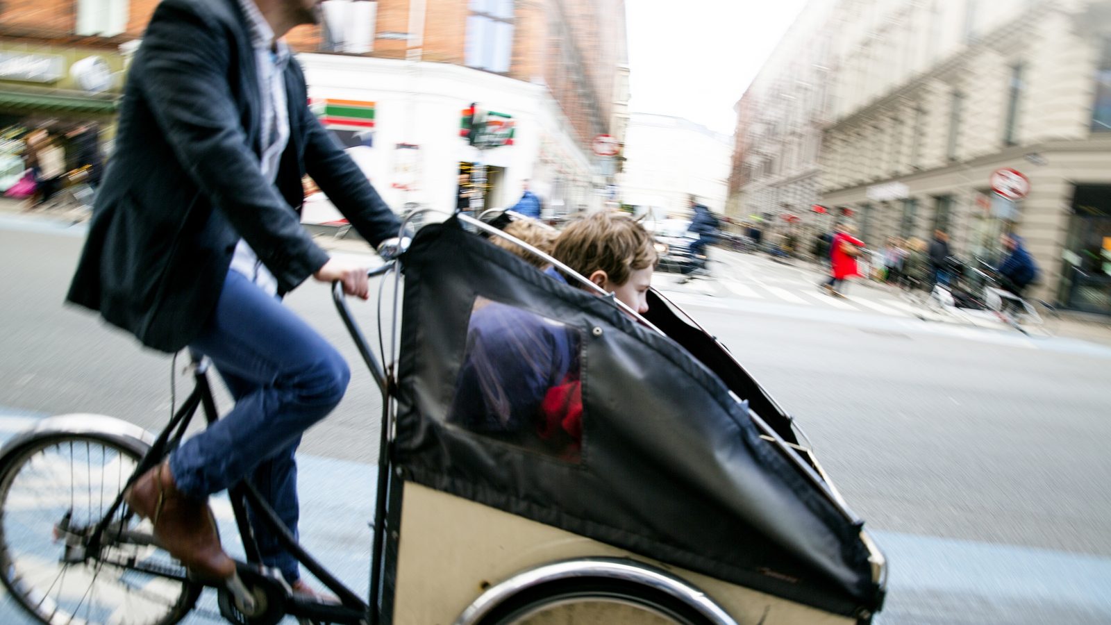 A parent cycling two children in a cargo bike through Copenhagen